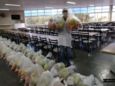 #PraTodosVerem imagem com um nutricionista de jaleco e máscara segurando uma cesta de produtos (verduras, legumes, frutas). As demais cestas estão organizadas no chão.