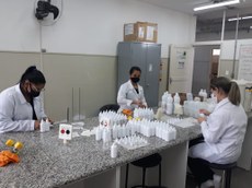 #Pratodosverem: três mulheres de jalecos brancos, e máscaras, fazendo álcool glicerinado 70%, na bancada de um laboratório.