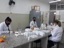 #Pratodosverem: três mulheres de jalecos brancos, e máscaras, fazendo álcool glicerinado 70%, na bancada de um laboratório.