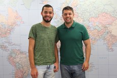 A foto mostra o estudante em pé ao lado do Diretor de Relações Internacionais e Interinstitucionais do IF Sudeste MG, com mapa mundi ao fundo.