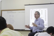 Professor com a imagem da sua apresentação ao fundo.