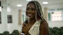 #Pratodosverem: Maria Luiza Magalhães fala com um microfone nas mão. Foto de Yuri Deslandes, tirada durante uma ação do Conselho Municipal da Juventude de Santos Dumont, no qual a estudante exerce a função de segunda secretária.