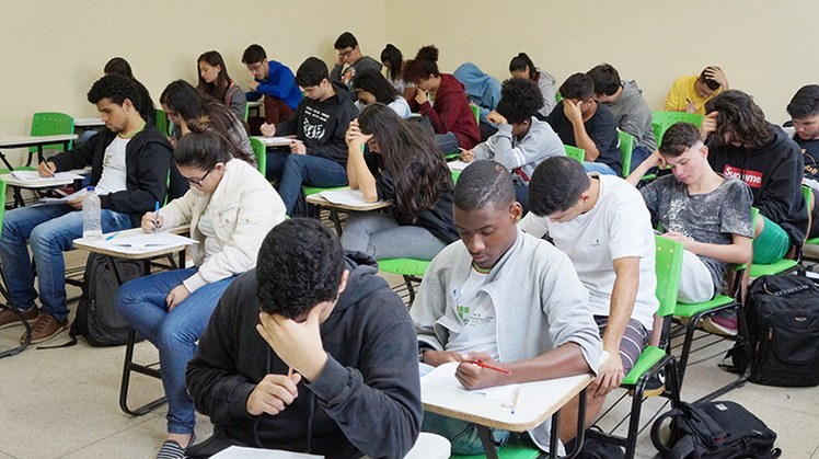 #Pratodosverem: Estudantes sentados em carteiras, realizando a prova do simulado do Enem. A sala está lotada.