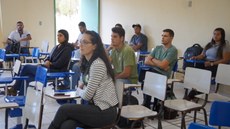 Estudantes sentados em carteiras olhando fixamente para frente. Ao fundo da foto, uma porta aberta.