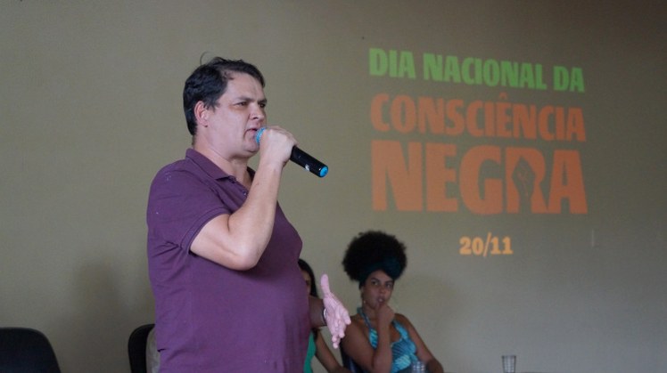 #Pratodosverem: O servidor Germano faz sua apresentação. Ele está com microfone na mão. Ao fundo, a projeção com o nome da data comemorativa.