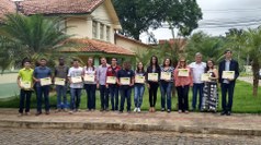 #Pratodosverem: Os premiados estão lado a lado, mostrando seus diplomas. Ao fundo, há jardim e parte do Prédio Administrativo.