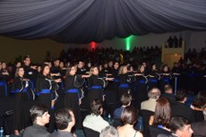 #Pratodosverem: Estudantes estão na solenidade de formatura. Eles usam becas, estão em pé e com o braço direito para frente, fazendo o juramento.