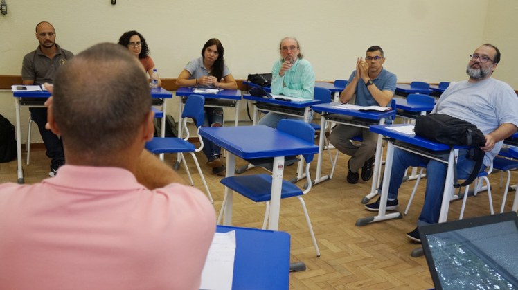 #Pratodosverem: professores sentados em carteiras de sala de aula em roda, discutindo o tema do grupo de trabalho.