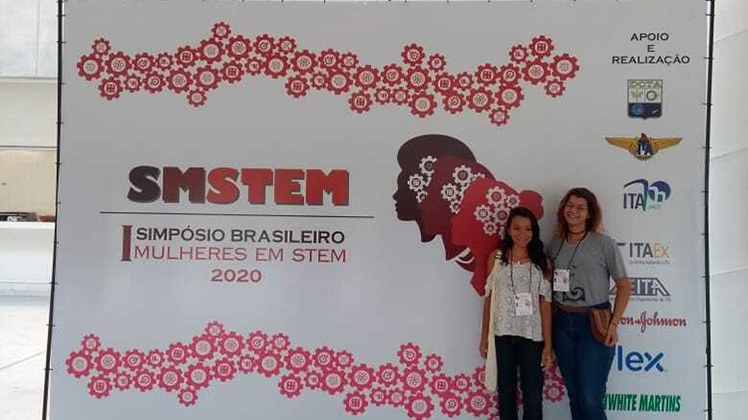 Meninas Digitais em Simpósio #Pratodosverem: As integrantes do projeto Meninas Digitais em frente ao banner do evento.