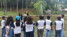 #pratodosverem: Imagem mostra alunas Camila e Crislene conversando com os estudantes de escolas municipais no Museu de Cabangu. Os estudantes estão de costas, observando as orientações das alunas, que aparecem de frente para a imagem. Ao fundo, o lado do Museu de Cabangu.