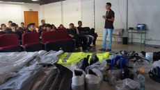 #pratodosverem: Imagem mostra meda com equipamentos de proteção individual. Ao fundo, técnico de Laboratório Igor Oliveira explica utilização deles aos alunos.                 