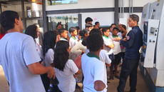 #pratodosverem: Imagem mostra técnico de laboratório Igor Oliveira conversando com estudantes do Polivalente próximo ao Centro de Usinagem por Comando Numérico Computadorizado (CNC), no Bloco 1 do Campus Santos Dumont do IF Sudeste MG.