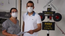 #pratodosverem: Imagem mostra coordenadora de Estágios do Campus Santos Dumont, Marcela Bertolin, e CEO da No Fake, João Carlos Souza. No Laboratório de Manutenção Ferroviária, eles estão segurando o contrato de parceria entre as instituições.