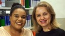 #pratodosverem: Imagem mostra bibliotecárias Paula Souza e Érica Veloso. Elas estão sorridentes. Ao fundo, aparece uma estante com livros na Biblioteca Acyr Loureiro Lima.                               