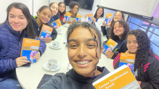 #pratodosverem: Imagem mostra estudantes do IF Sudeste MG e bibliotecária Paula Souza em torno da mesa de sala de estudo da Biblioteca Acyr Loureiro Lima. Elas estão segurando o livro "Contos Tradicionais do Brasil", de Luís da Câmara Cascudo.