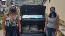#pratodosverem: Imagem mostra representante da Sociedade São Vicente de Paulo ao lado da professora Francilene Barbosa, do IF Sudeste MG. As duas estão em pé e usando máscara. Entre elas, um carro com o porta-malas aberto e com alimentos e kits de higiene destinados a famílias.