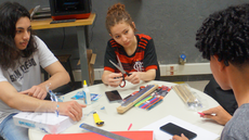 #pratodosverem: Imagem mostra trabalho desenvolvido em conjunto por estudantes do curso técnico em Automação Industrial e participantes da oficina. Eles estão sentados a uma mesa circular, com diversos materiais simples para a confecção de protótipos.