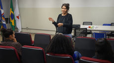 #pratodosverem: Imagem mostra colaboradora externa do projeto, Natália Reis, apresentando filmes da última sessão do Cine Neabi, no Auditório do Campus Santos Dumont.