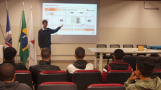 #pratodosverem: Imagem mostra engenheiro Geraldo Paticcie no Auditório do Campus Santos Dumont. Ele está se dirigindo aos estudantes, que estão sentados e de frente para o palestrante, durante apresentação. Ele aponta para a tela para uma explicação sobre o conteúdo.