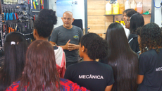 #pratodosverem: Imagem mostra grupo de estudantes do curso técnico em Mecânica acompanhando apresentação de Sávio Nery em sua oficina de manutenção de bicicletas. Eles estão diante de um painel com ferramentas.