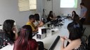 #pratodosverem: Imagem mostra estudantes do IF Sudeste MG sentados em torno de uma mesa, sobre a qual estão diversos equipamentos relacionados a fotografia. O técnico em audiovisual Alexandre Vargas, que ministrou o minicurso, conversa com os alunos. Foto: Leonardo Jardel.
