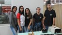 #pratodosverem: Imagem mostra cinco estudantes do curso técnico em Eletrotécnica durante apresentação da Feira de Ciências. Eles estão em pé, em frente a uma mesa com o equipamento construído pela equipe.