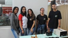 #pratodosverem: Imagem mostra cinco estudantes do curso técnico em Eletrotécnica durante apresentação da Feira de Ciências. Eles estão em pé, em frente a uma mesa com o equipamento construído pela equipe.