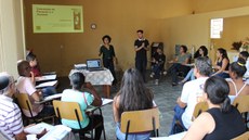 #pratodosverem: A imagem mostra a servidora Iara Nascimento e o bolsista Samuel Ribeiro conversando com moradores em atividade do projeto "Destino Formoso". Os moradores estão sentados em cadeiras dispostas em formato de semicírculo e observam a apresentação.