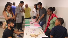 #pratodosverem: Imagem mostra estudantes, professores e convidados interagindo em torno de uma bancada com os jogos didáticos de Matemática