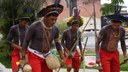#pratodosverem: Imagem mostra integrantes do grupo Sabuká Kariri-Xocó durante apresentação de dança em praça pública em Santos Dumont. Eles estão em pé e vestidos com roupas e acessórios característicos do grupo.