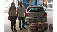 #pratodosverem: Imagem mostra coordenadora do subcomitê local de enfrentamento à Covid-19 no Campus Santos Dumont, professora Francilene Barbosa, e representante do Cras Edir Ramos de Faria. Os dois estão em pé, de máscara e ao lado de cestas destinadas à instituição e de um veículo. No fundo, aparece o painel artístico em homenagem ao Pai da Aviação, no Campus Santos Dumont do IF Sudeste MG