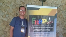 Imagem mostra professor Gabriel Conceição em pé. À direita, aparece um banner do 4º Encontro Nacional de Pesquisa em História da Educação Matemática, realizado na Universidade Federal do Mato Grosso do Sul (UFMS) em 2018. Foto: Gabriel Conceição (arquivo pessoal).