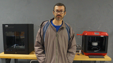 #pratodosverem: Imagem mostra estagiário Roberto Jardim, em pé, à frente de uma bancada com duas impressoras 3D no Laboratório IFMaker.