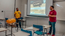 #Pratodosverem: João Victor Pereira Pimentel, membro do LAPSIQ, está de pé, em frente a um projetor, proferindo palestra.