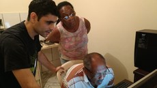 #Pratodosverem: imagem traz um idoso (sentado na frente do computador) e uma idosa (de pé e olhando para o computador) e o professor reclinado explicando algo ao aluno durante edição anterior do Projeto InForUbá.