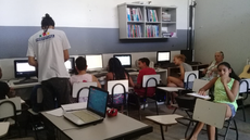 Alunos sentados em frente a computadores. Instrutor em pé.